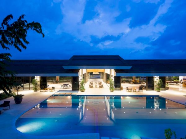 A luxurious, illuminated pool with a modern building in the background under a twilight sky.