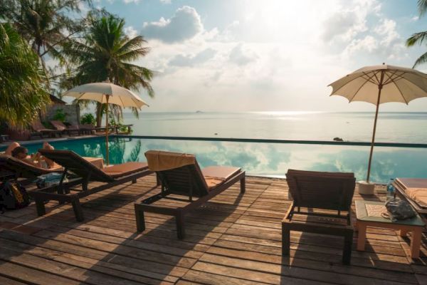 A serene poolside scene with lounge chairs and umbrellas overlooking a calm, reflective body of water under a partly cloudy sky.