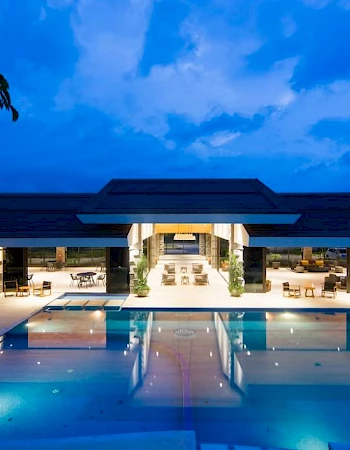 This image shows a luxurious outdoor swimming pool at night, with a modern building in the background and ambient lighting.