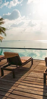 A serene poolside with lounge chairs, parasols, and a view of the ocean under a sunny sky.