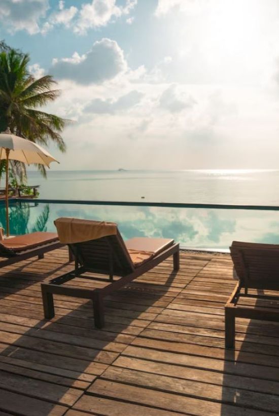 A tranquil poolside scene with lounge chairs, umbrellas, and a view of the ocean under a partly cloudy sky.