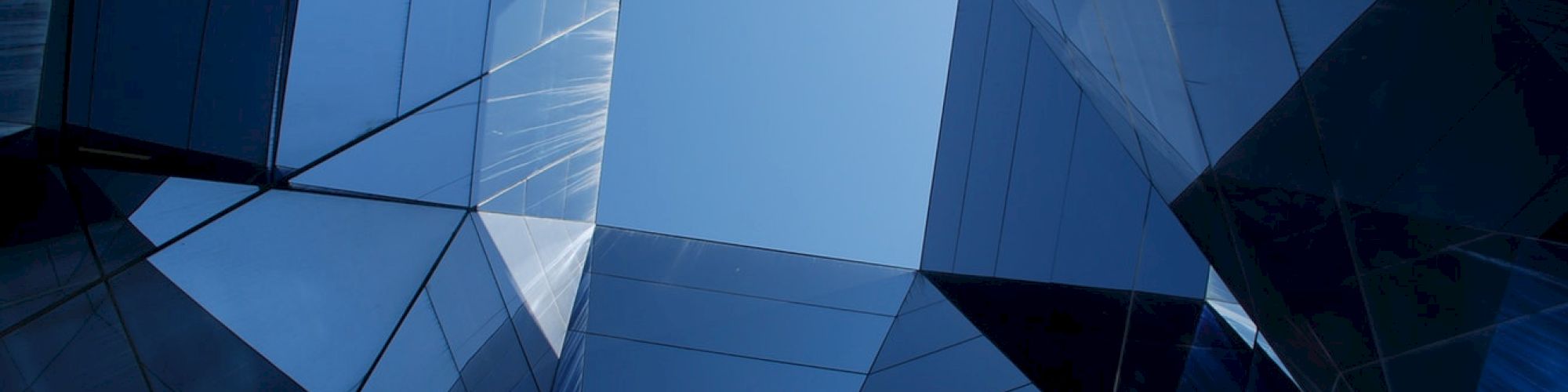 The image shows a perspective view looking up at the sky through geometric glass buildings, creating a kaleidoscope effect.