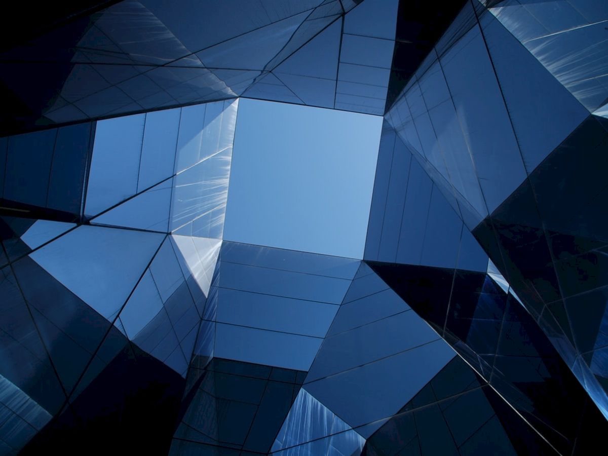 Geometric glass structures form an abstract, angular pattern against the sky, using reflective surfaces to play with light and shadow.