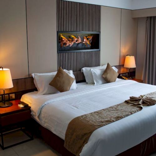 A neatly arranged hotel room with a large bed, decorative pillows, bedside lamps, and curtains.