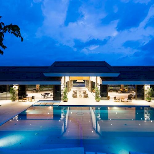 A luxurious pool area with a modern, open building in the background, under a twilight sky, creating a serene atmosphere.