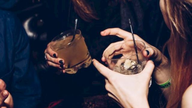 People are enjoying drinks at a social gathering, laughing and gesturing with their hands.