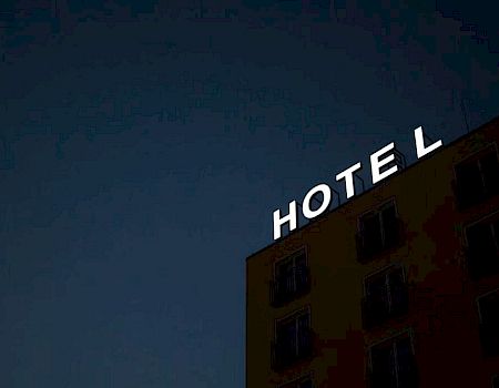 A building with a sign reading "HOTEL," missing the letter "L," against a dark sky.