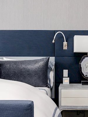A modern bedroom features a bed with navy pillows, a stylish lamp on a nightstand, and a sleek wall-mounted reading light.