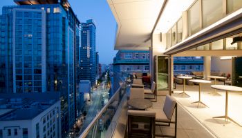 Rooftop terrace with modern seating, overlooking a cityscape with tall buildings at dusk. Cozy ambiance.