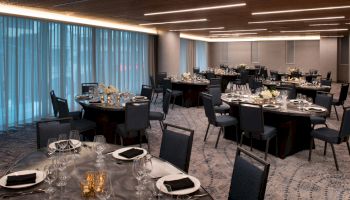 The image shows an elegant banquet hall with round tables set for an event, featuring floral centerpieces and neatly arranged tableware.