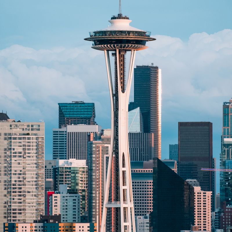 The image shows the Space Needle in Seattle, with a city skyline in the background, under a clear sky.