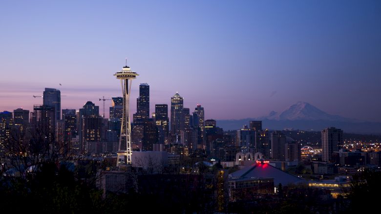 Seattle skyline at dusk with the Space Needle and Mount Rainier in the background, lit city lights against a twilight sky.
